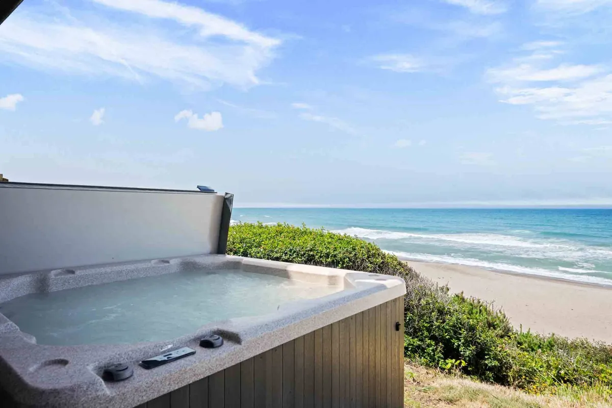A tranquil scene showing a private hot tub nestled on a deck, surrounded by lush greenery with a direct, unobstructed view of the ocean. The ambiance is intimate and nature-inspired, ideal for peaceful moments like stargazing or watching sunsets over the water.