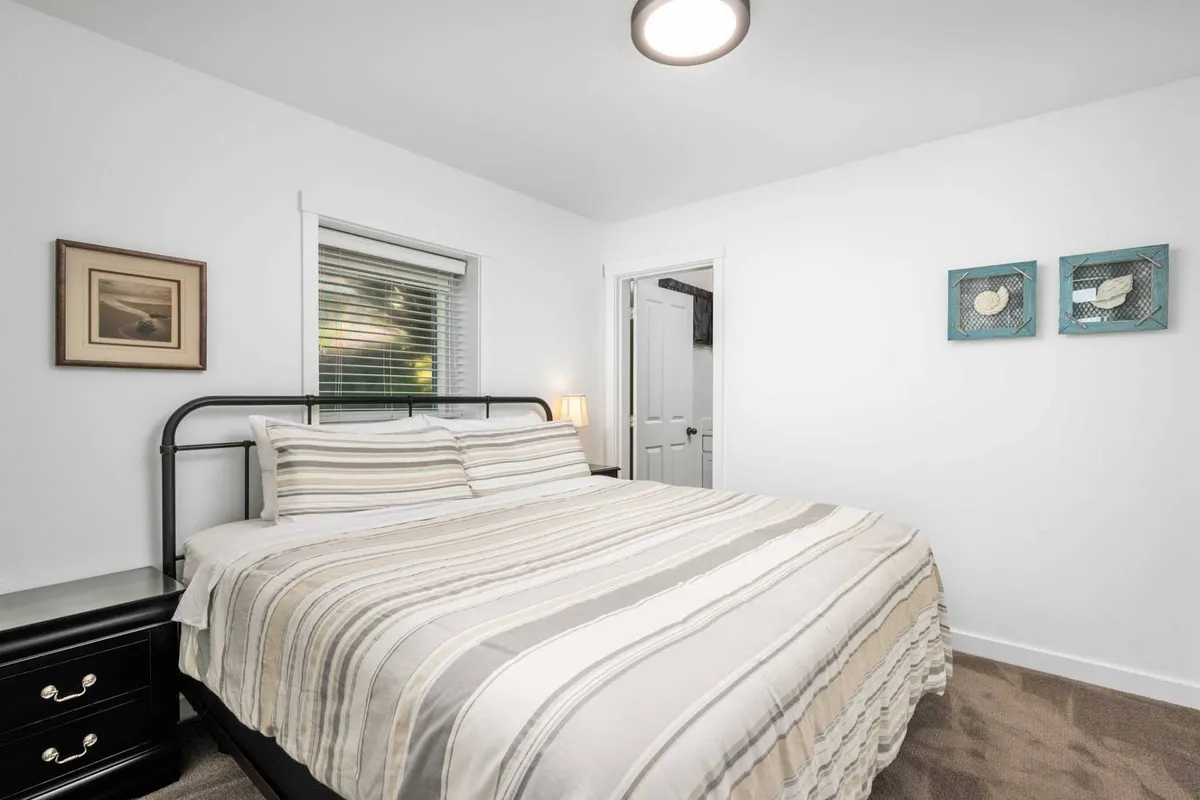 A bright, inviting bedroom with a comfortable bed, a nightstand, and soothing artwork. Sunlight streams in, creating a warm, restful environment.
