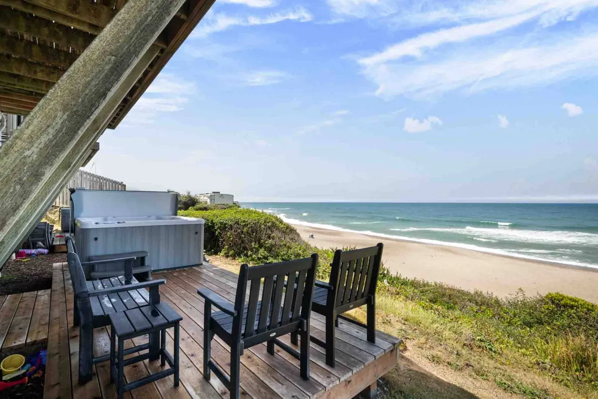 This scene showcases a spacious beachfront deck with a comfortable outdoor seating area and a hot tub overlooking the ocean. The setting is perfect for gatherings, morning coffee, or intimate conversations as described in the narrative.