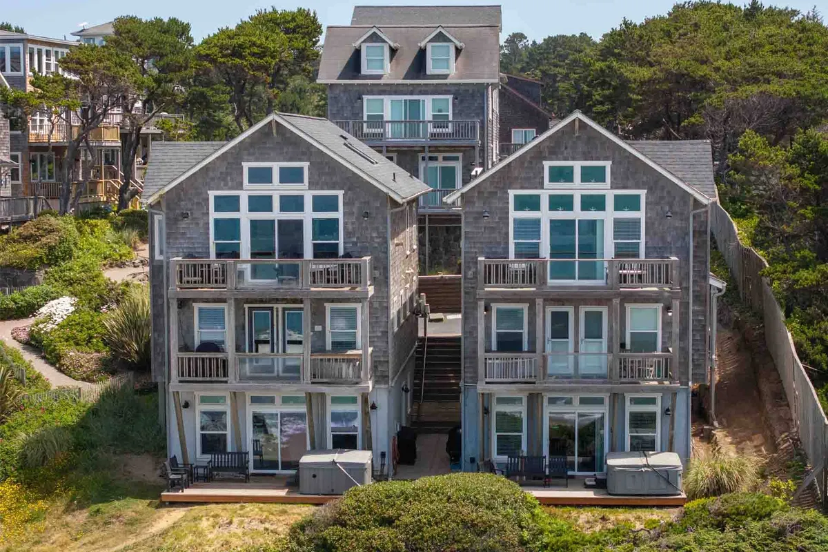 This exterior view features two large, glass-fronted houses with balconies, surrounded by greenery, and a staircase leading directly to the sandy beach. The scene evokes a sense of openness and easy access to outdoor adventures, perfect for pet walks and family time.