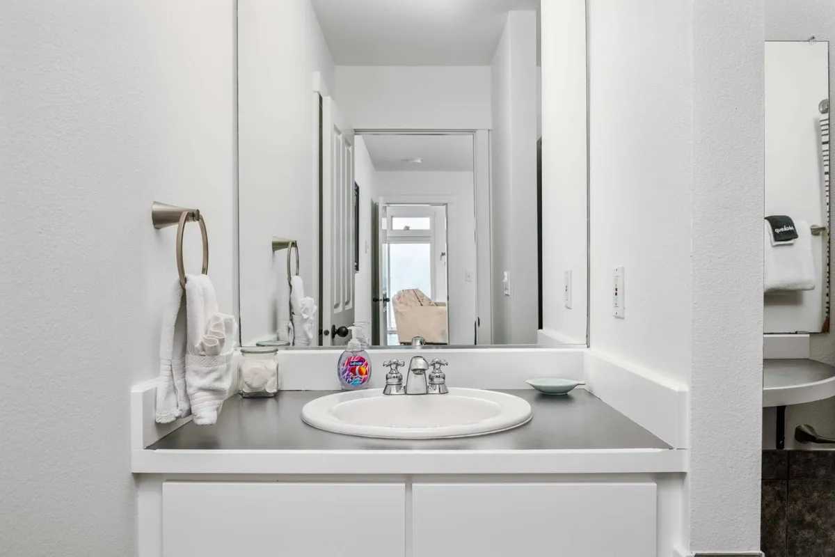 A modern, tranquil bathroom featuring a sleek sink, mirror, fresh towels, and decorative touches. The space is inviting, perfect for morning or evening routines.