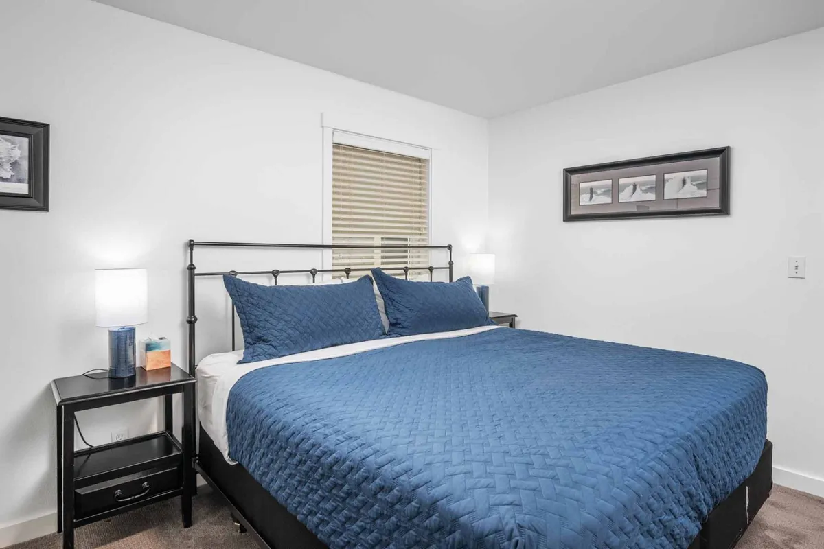 A serene bedroom featuring a king-size bed with soothing blue bedding, flanked by nightstands with lamps. Framed coastal artwork adorns the walls, creating a peaceful retreat ideal for restful sleep.