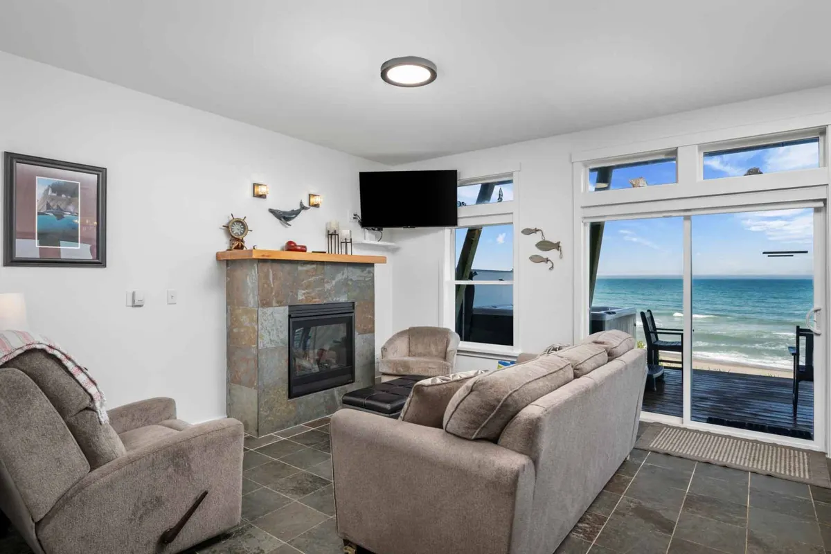 A cozy seating area with a fireplace and large windows offering sweeping views of the ocean. Comfortable couches and chairs are arranged for easy conversation or quiet relaxation, embodying a tranquil, welcoming retreat atmosphere.
