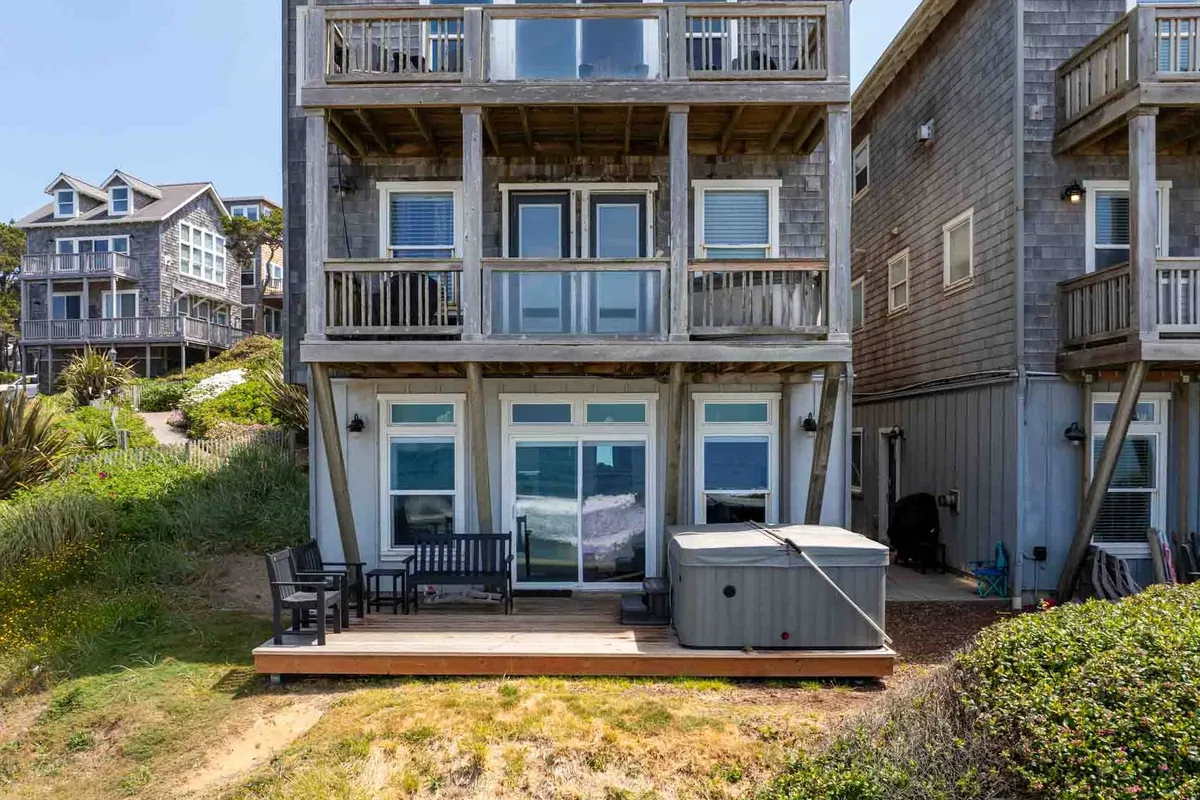 An exterior view of a balcony with comfortable seating and an inviting hot tub, overlooking the ocean through large glass doors. The setting is calm, with the promise of relaxation while enjoying the ocean view and fresh air.