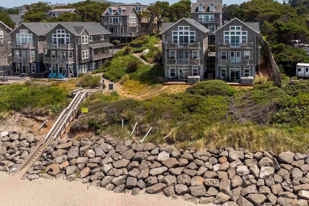 An inviting exterior view showcases several beachfront homes with well-kept green landscaping along a rocky shoreline. The image conveys a tranquil, community-oriented atmosphere, where residents and guests can enjoy the natural beauty of the coast, ideal for morning walks with pets.